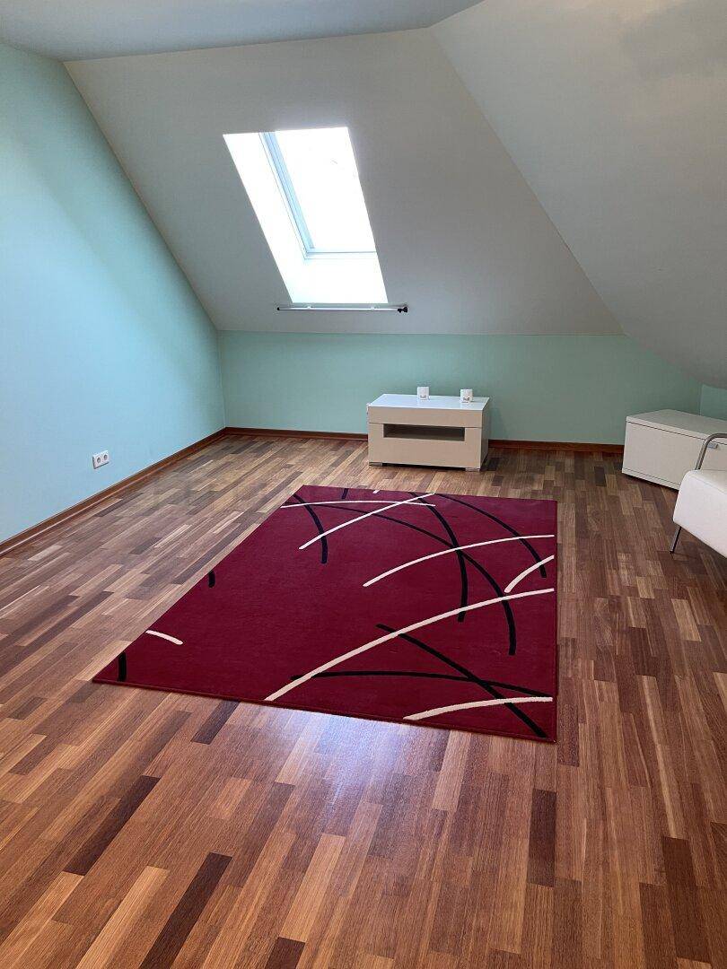 Geräumiges Dachgeschosszimmer mit Holzboden, Dachfenster und einem farbigen Teppich.