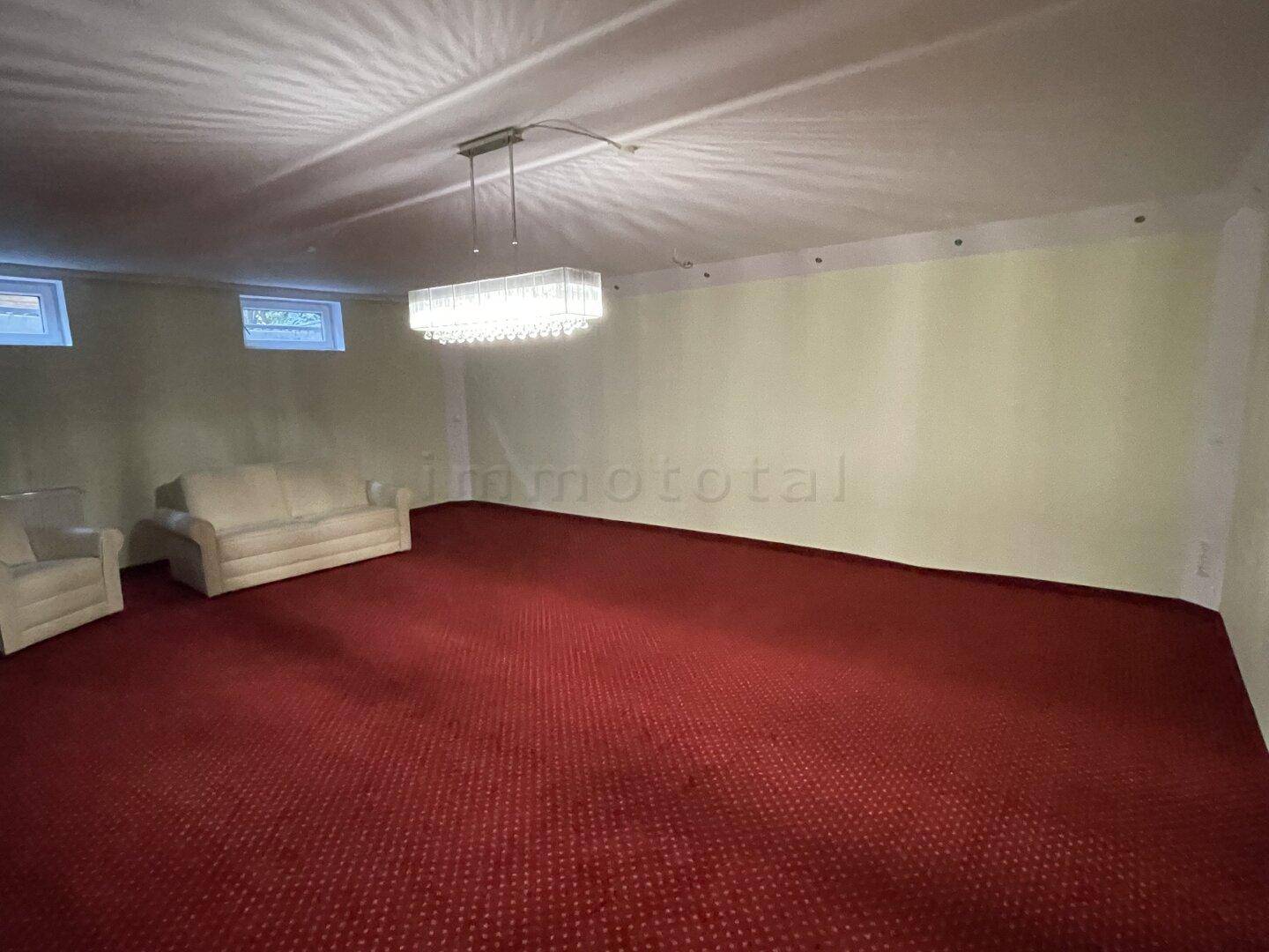 Geräumiger Raum mit rotem Teppichboden, kleinen Fenstern und einem eleganten Kronleuchter.