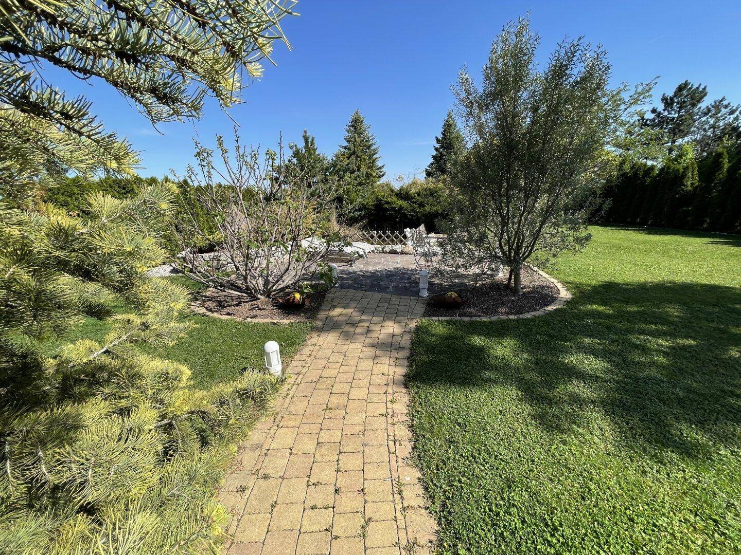 Idyllischer Gartenweg führt zu einem runden Sitzbereich, umgeben von Bäumen und Sträuchern.