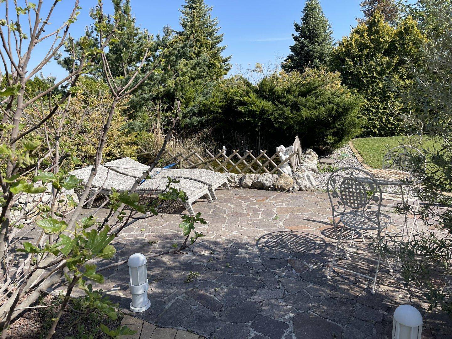 Gemütliche Steinterrasse mit Liegestühlen und einem kleinen Teich, umgeben von üppigem Grün.