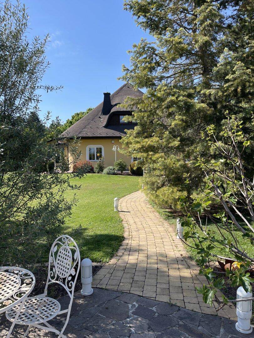 Charmantes Haus mit besonderem Dach, umgeben von einem weitläufigen, grünen Garten.