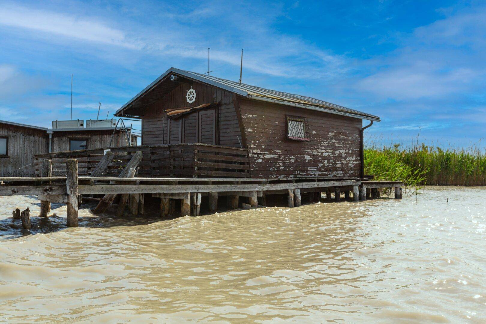 Nahaufnahme eines rustikalen Holzhauses auf Stelzen über dem Wasser mit verwitterter Holzfassade.