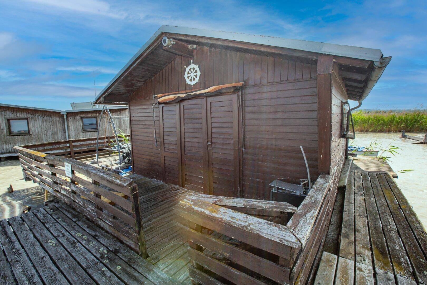 Rustikales Holzhaus mit einer Holzterrasse, Eingangstür und einem dekorativen Steuerrad an der Fassade.