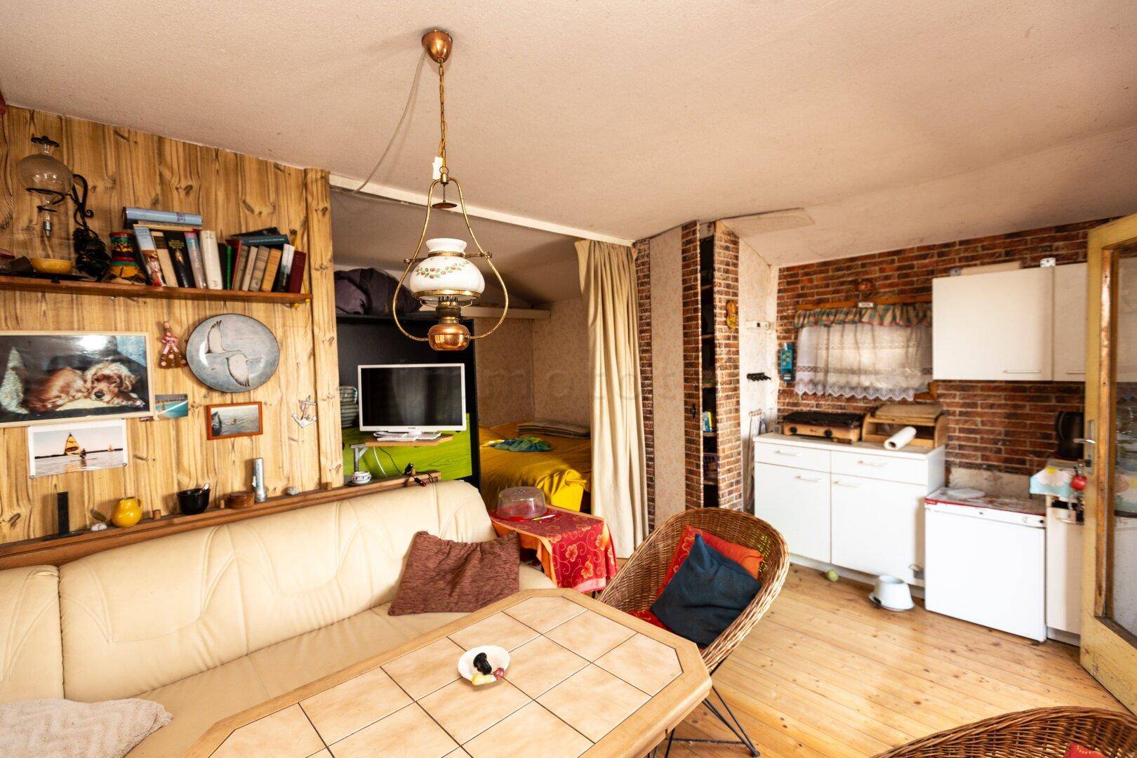 Offener Wohnbereich mit Holzwänden, kleiner Küchenzeile und Blick in ein angrenzendes Schlafzimmer.