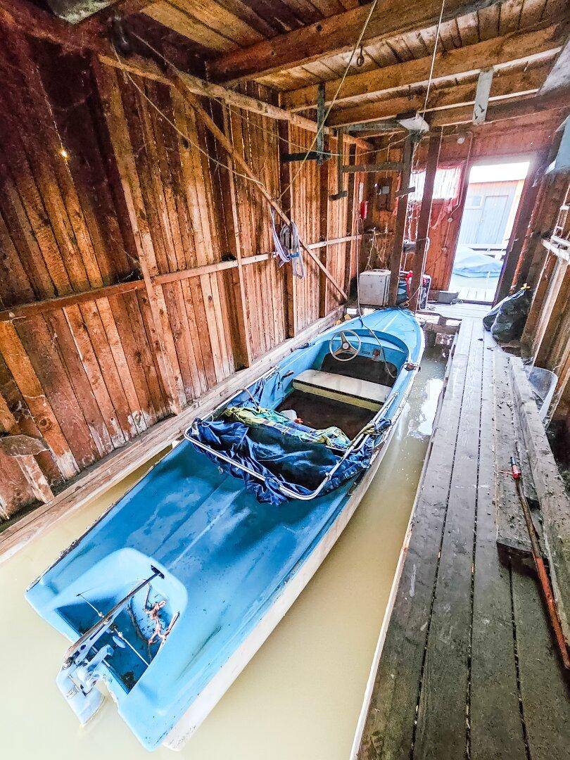 Innenansicht eines Bootshauses mit einem blauen Boot im Wasser und rustikalen Holzwänden.