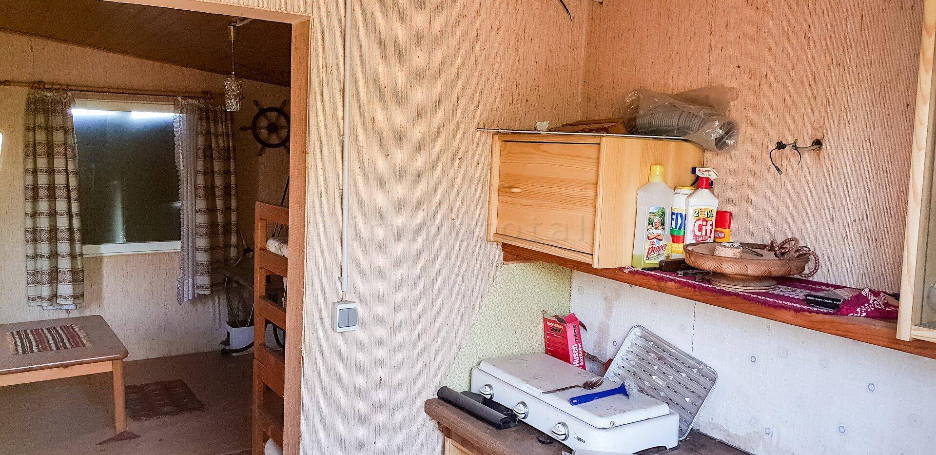 Einfache Küchenzeile in einer Hütte mit rustikaler Wandverkleidung und Blick in den Wohnbereich.