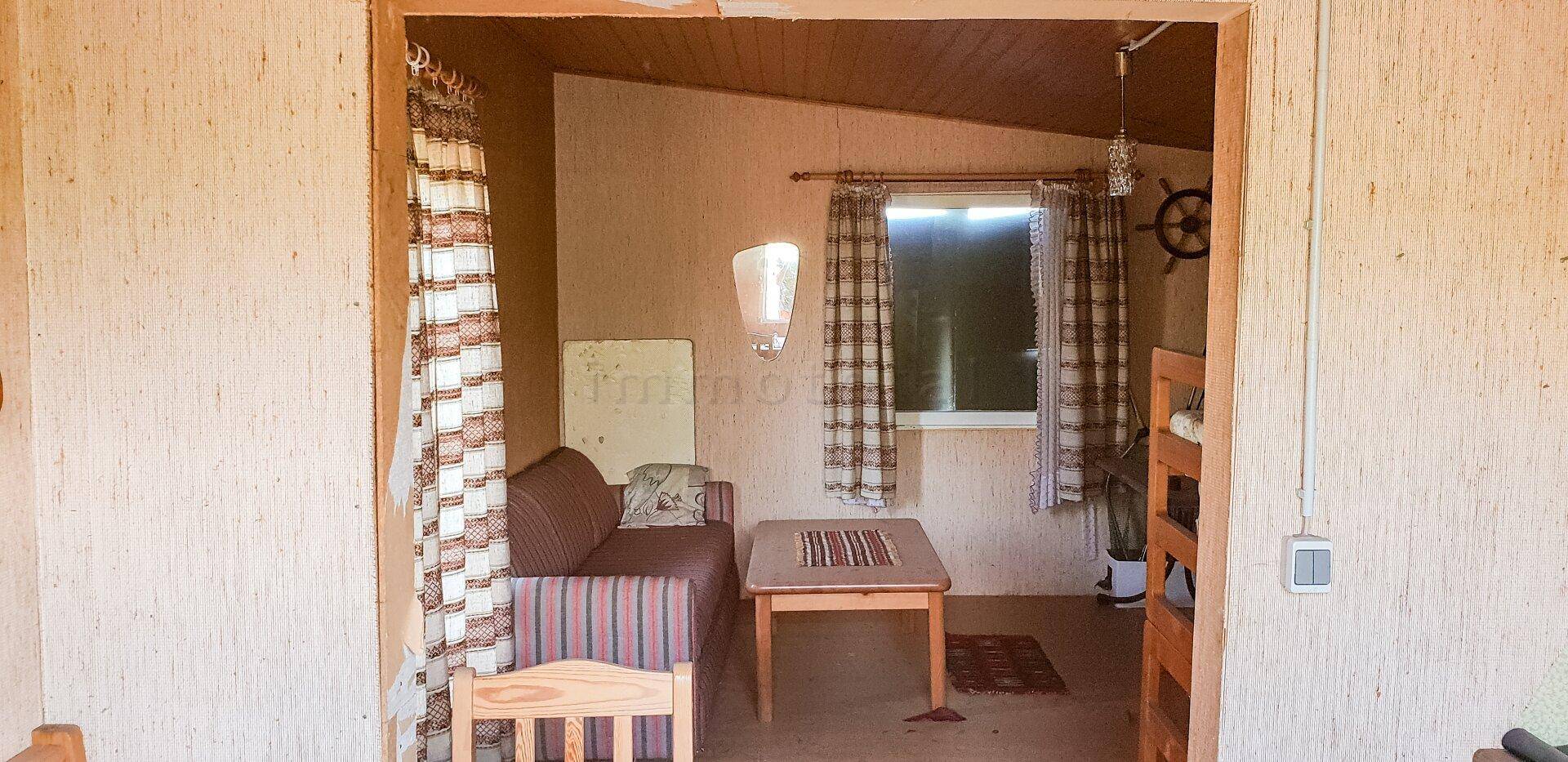 Gemütlicher Wohnbereich in einer Hütte mit Sofa, kleinem Tisch und karierten Vorhängen am Fenster.