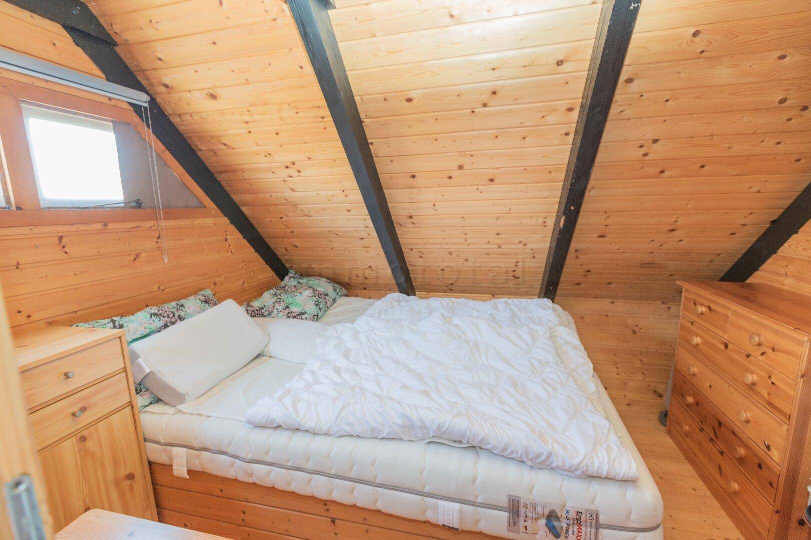 Schlafbereich mit Holzwänden, Dachschrägen und einem Bett auf einer Holzplattform in rustikalem Stil.