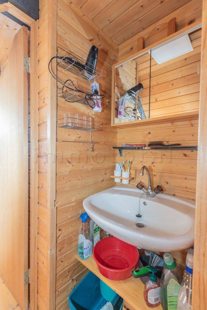 Kleines Badezimmer mit Holzwänden, Waschbecken und Spiegelschrank, funktional eingerichtet.