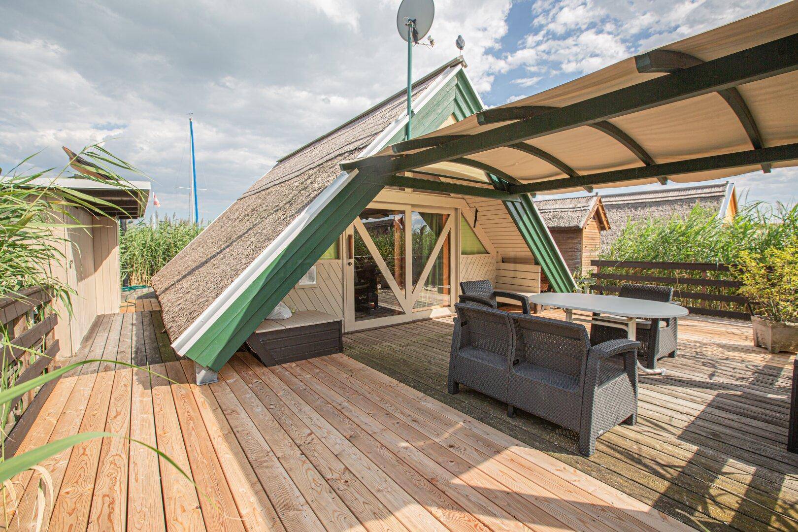 Geräumige Holzterrasse mit Sitzgelegenheiten und Blick auf das Reetdachhaus und die Umgebung.