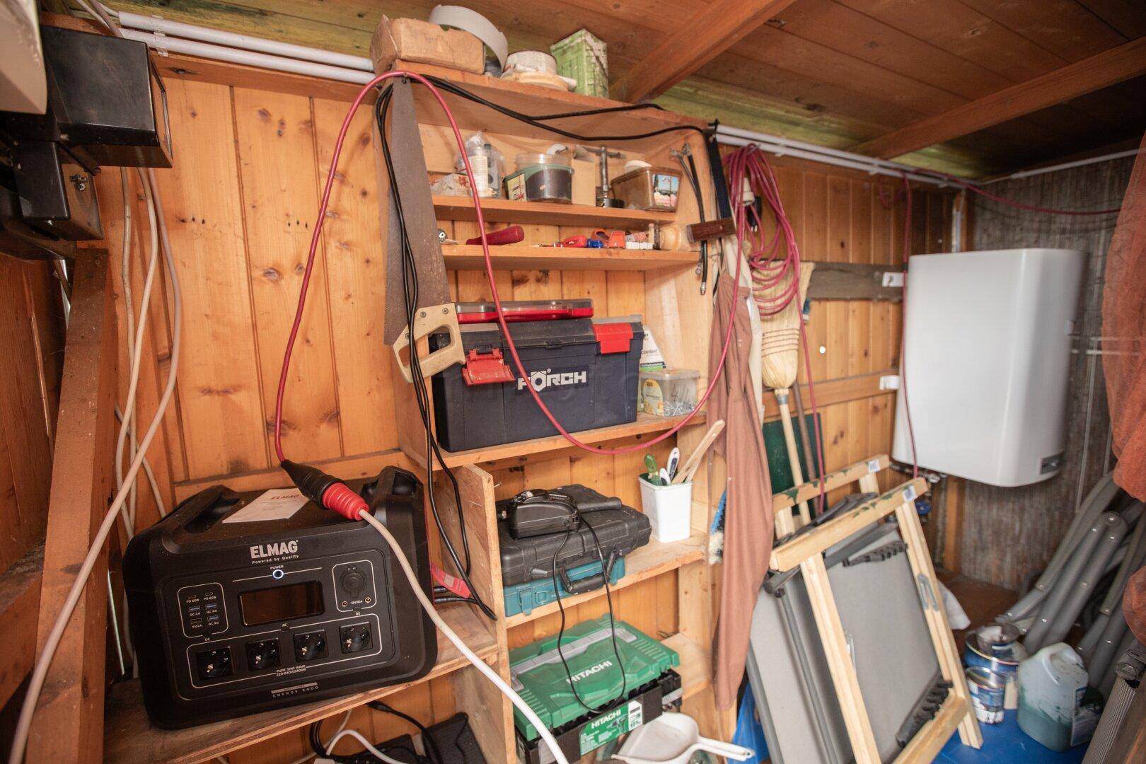 Innenansicht eines Geräteschuppens mit Werkzeugen, Regalen und elektrischen Installationen.