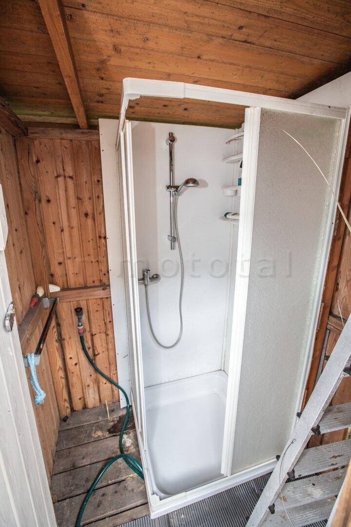 Einfache Duschkabine in einem Nebengebäude mit Holzwänden, funktional und praktisch.