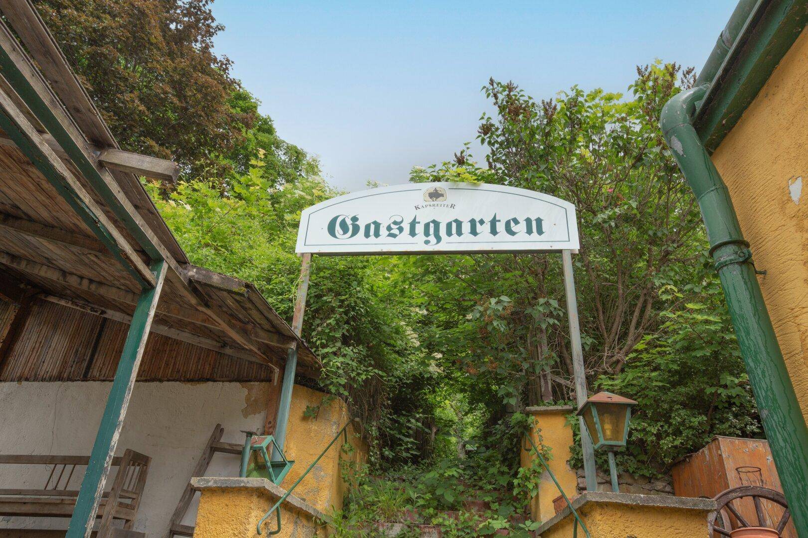 Eingangsbereich zu einem Gastgarten mit Treppe und üppiger Vegetation.