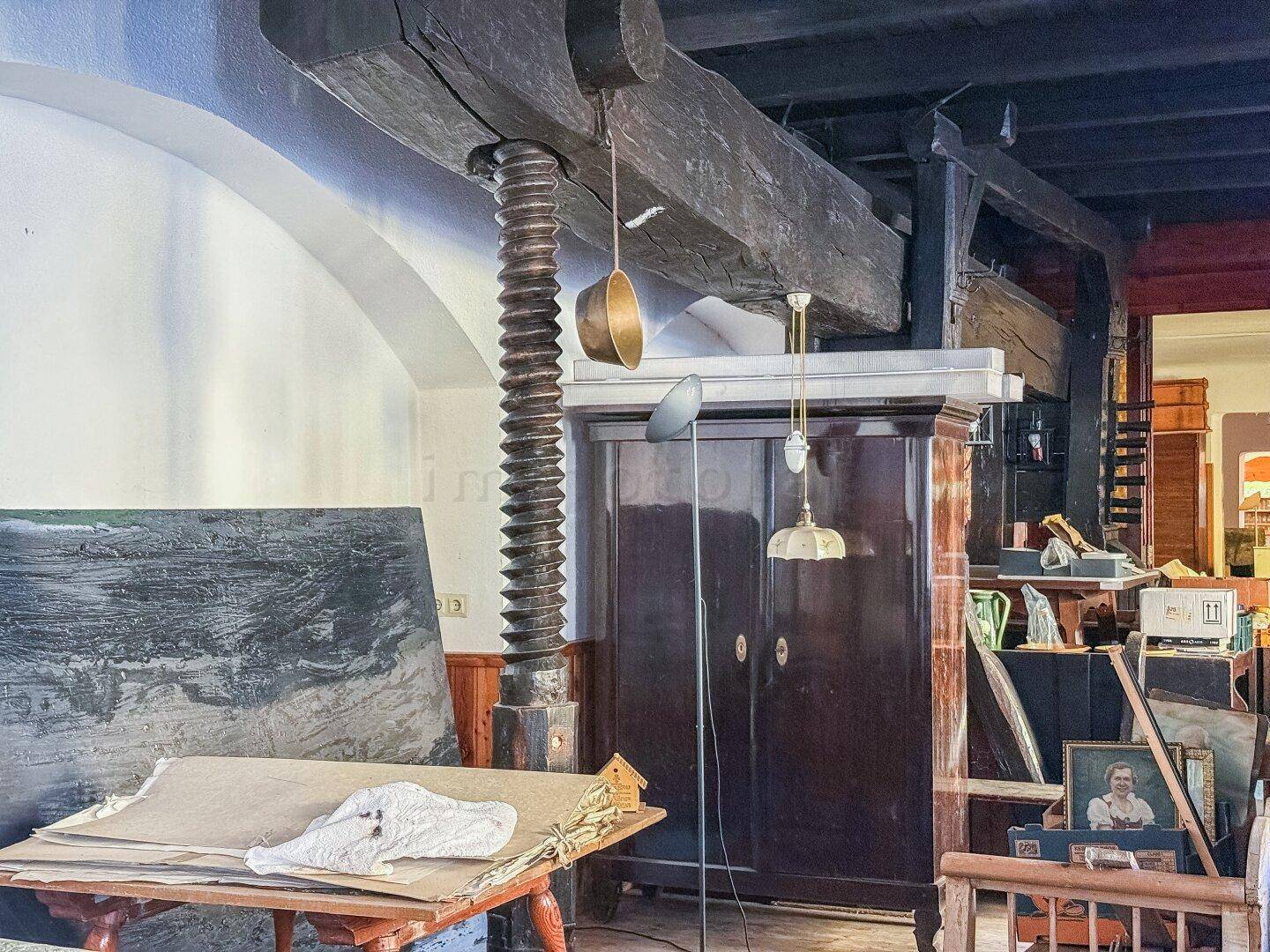 Innenraum mit historischer Holzpresse, alten Möbeln und dunkler Holzbalkendecke.