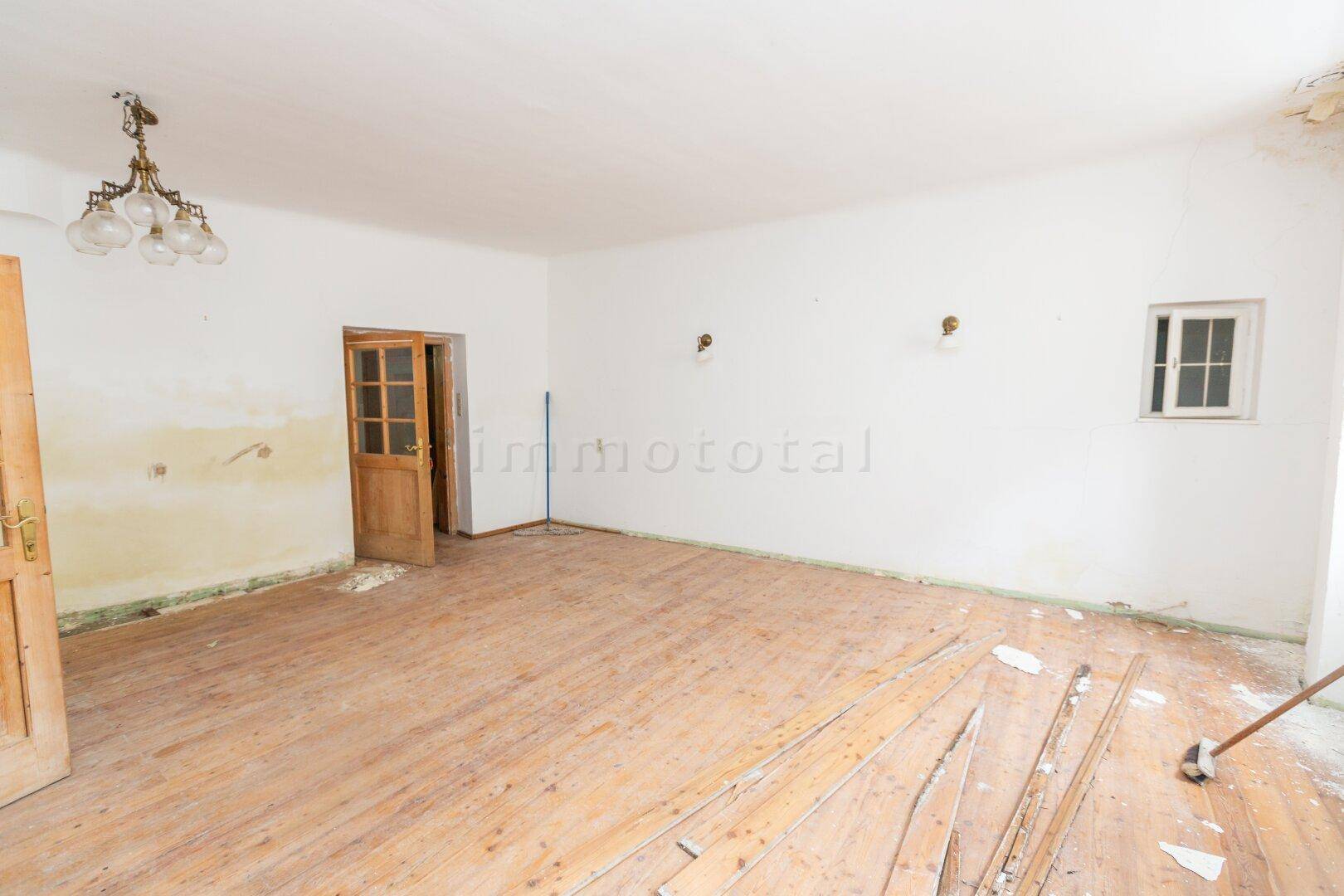 Leerer Raum mit Holzdielenboden, weißen Wänden und Renovierungsbedarf.