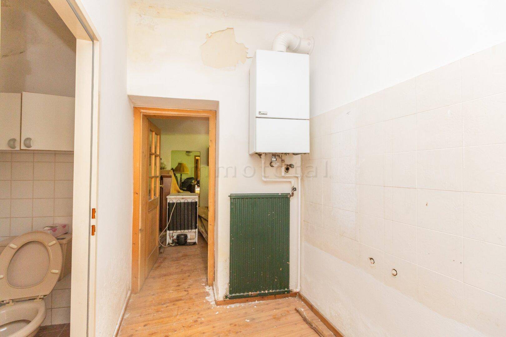 Kleiner Raum mit Gastherme, Heizkörper und Zugang zu einem WC-Bereich.