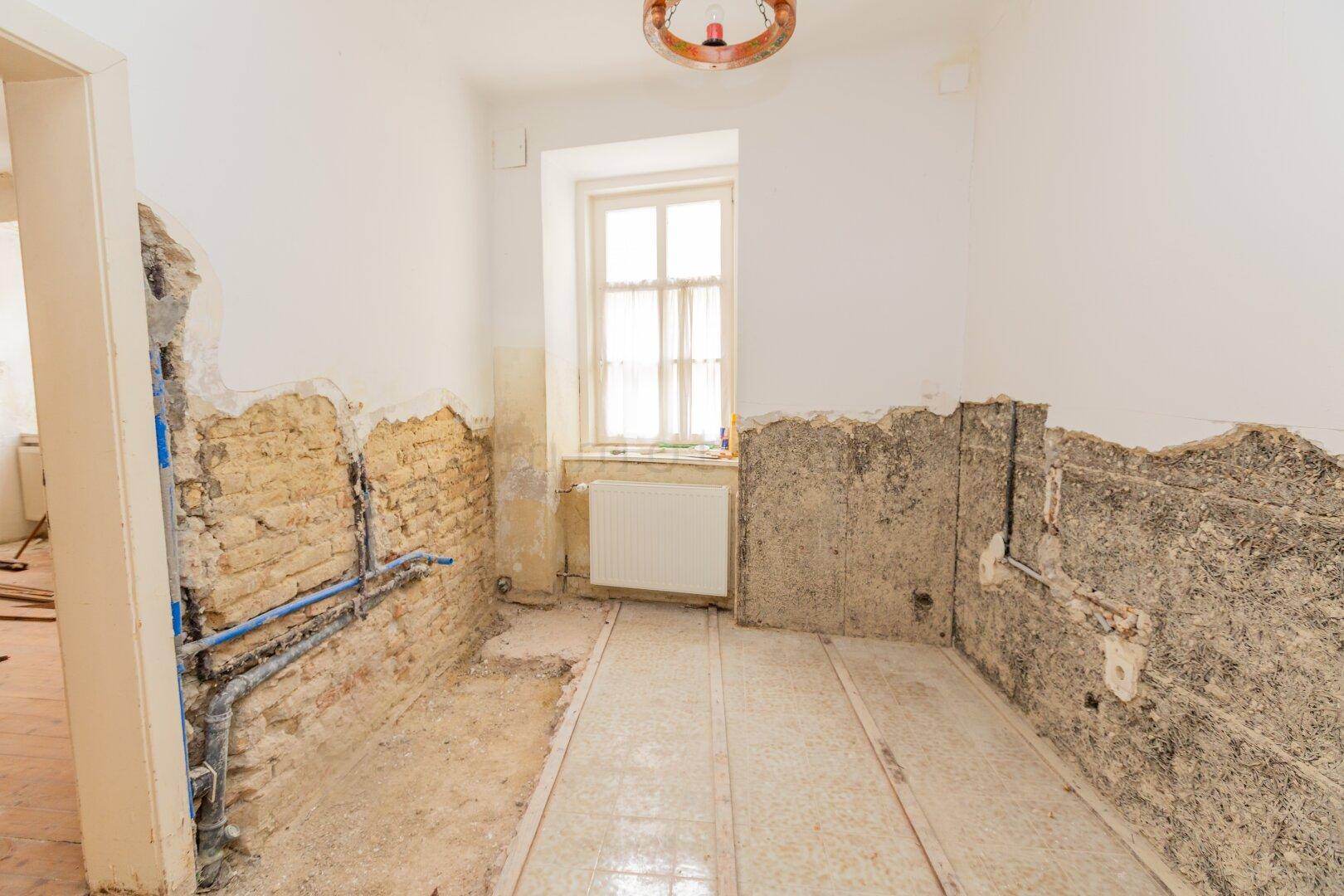 Raum in Renovierung mit freigelegten Ziegelwänden, Rohren und Fenster.
