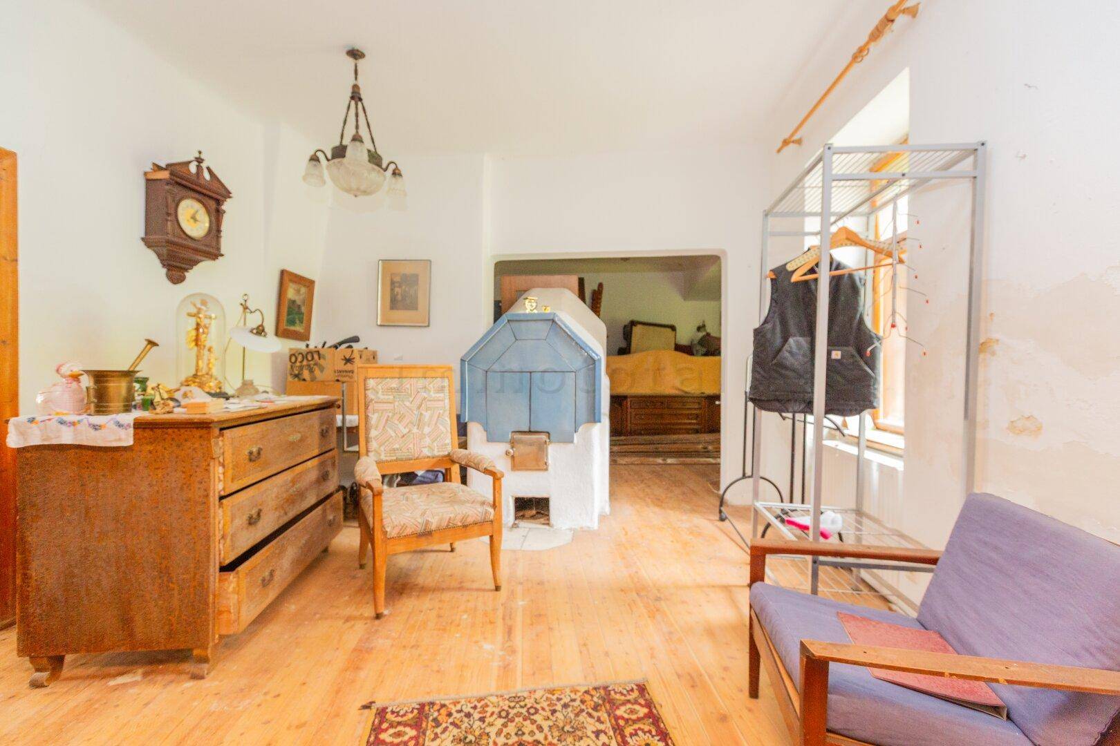 Gemütlicher Wohnraum mit traditionellem Kachelofen, Holzdielenboden und Vintage-Möbeln.