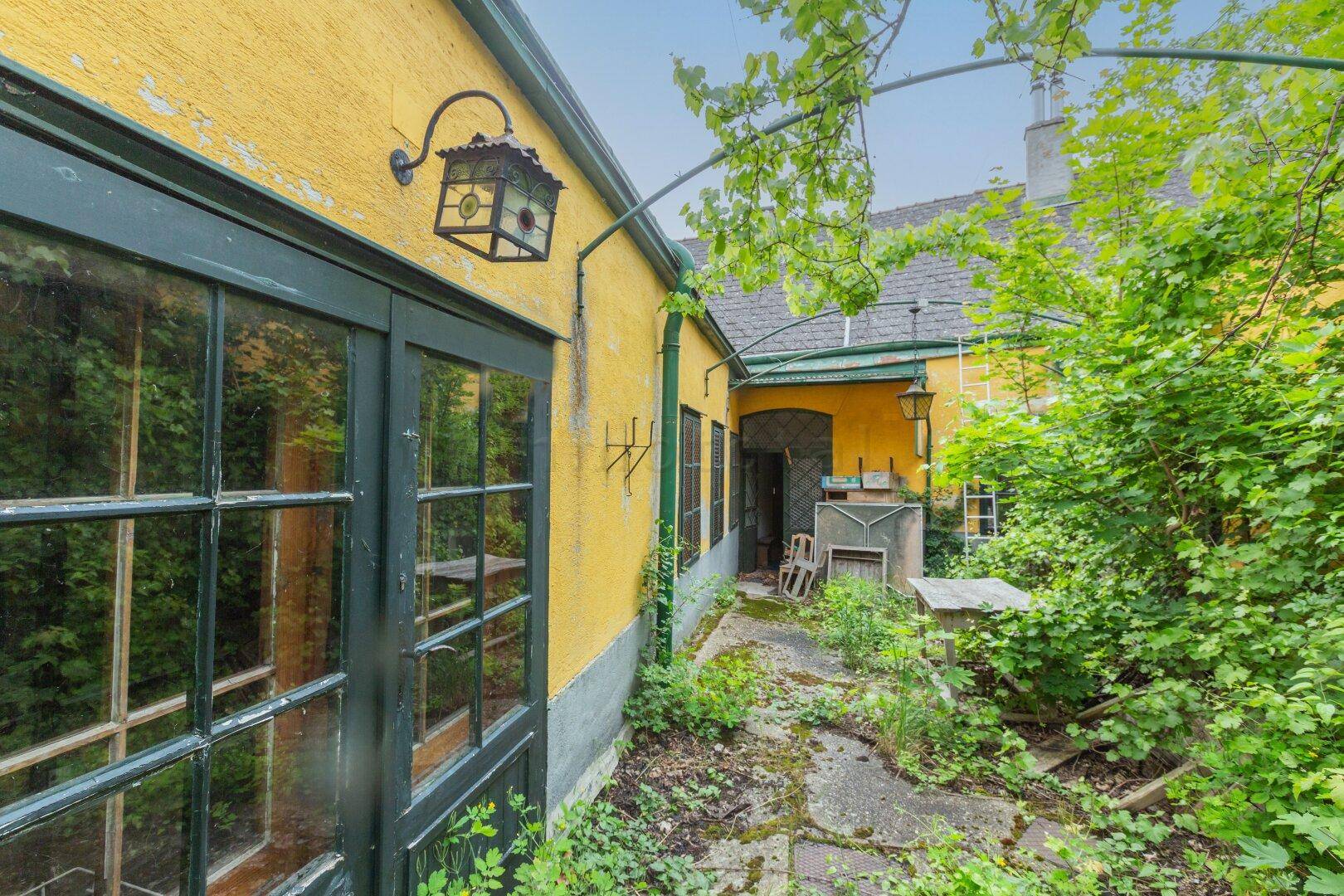 Seitenansicht eines alten Gebäudes mit gelber Fassade und zugewachsenem Weg.