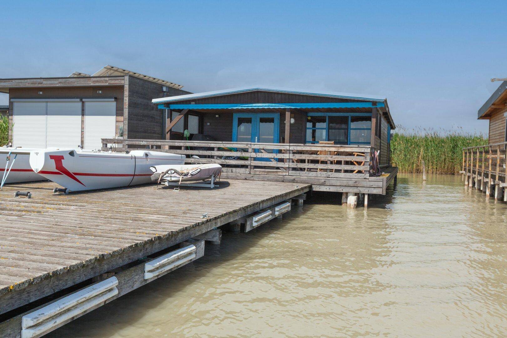 Holzhaus auf Stelzen mit großer Holzterrasse und Booten am Seeufer.