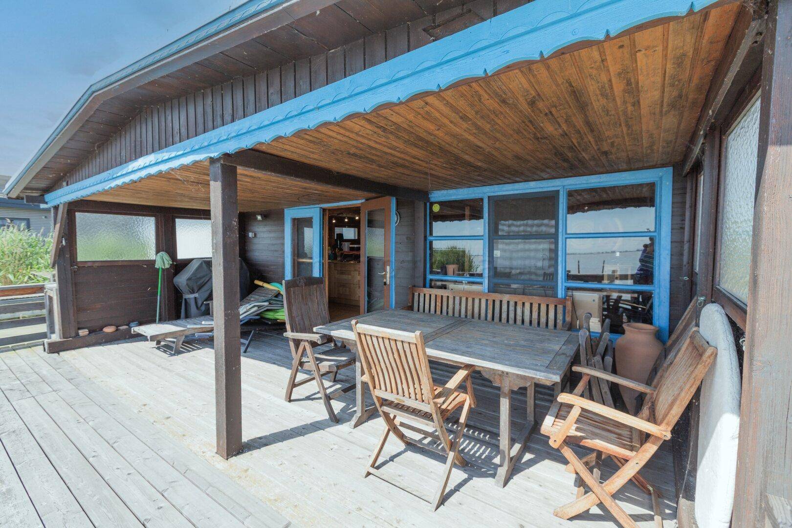 Überdachte Holzterrasse mit rustikalen Gartenmöbeln und Blick auf das Wasser.