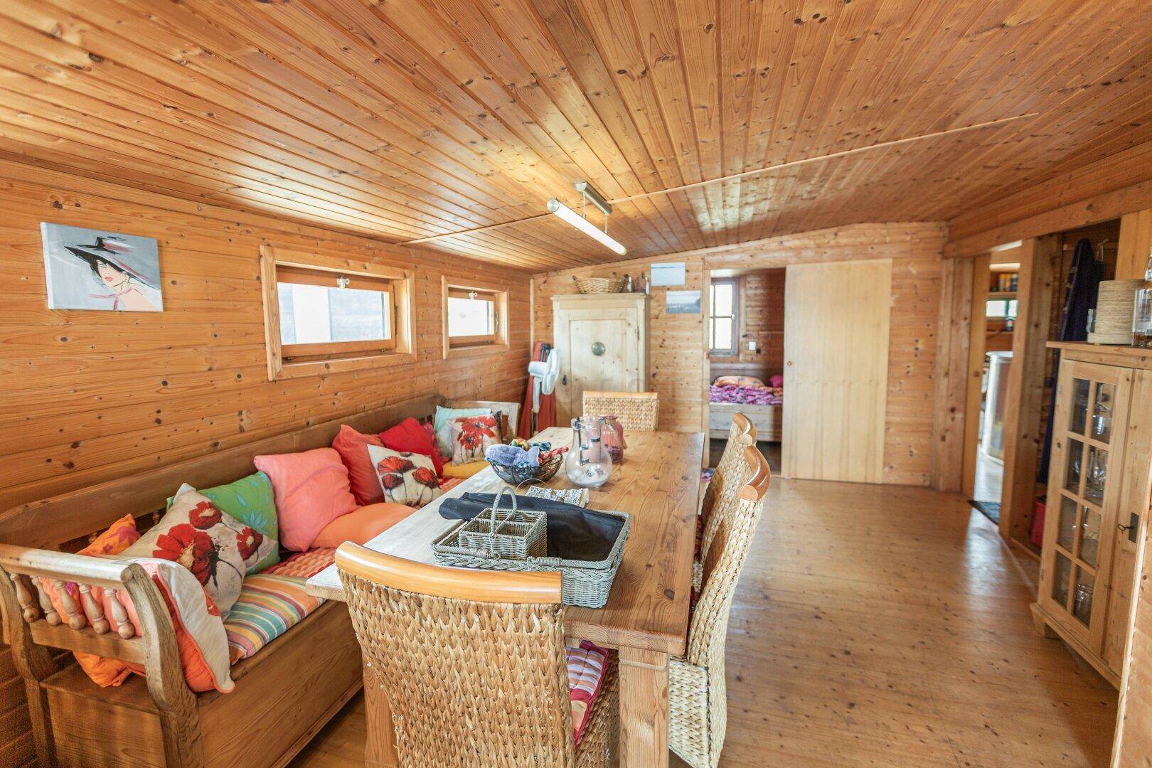 Gemütlicher Essbereich mit Holztäfelung, langer Sitzbank und bunten Kissen.