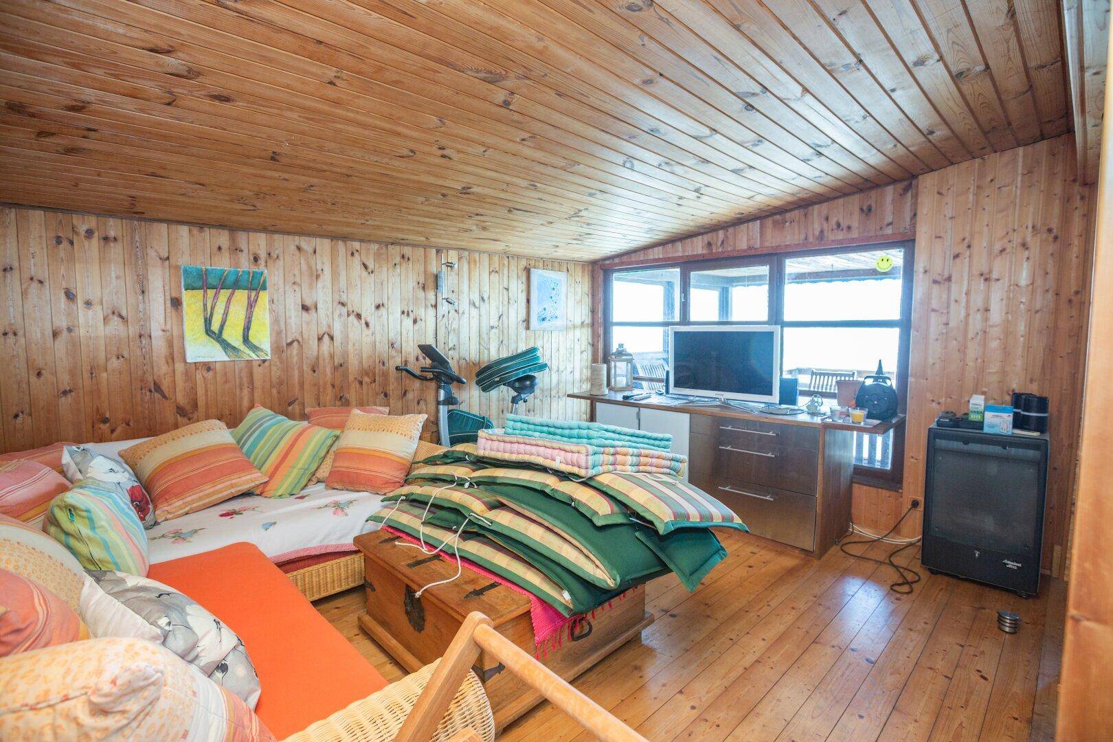 Wohnbereich mit Holztäfelung, Fernseher und großen Fenstern mit Seeblick.