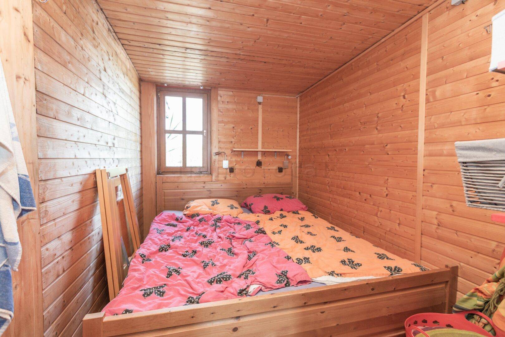 Gemütliches Schlafzimmer mit Holztäfelung, Doppelbett und kleinem Fenster.