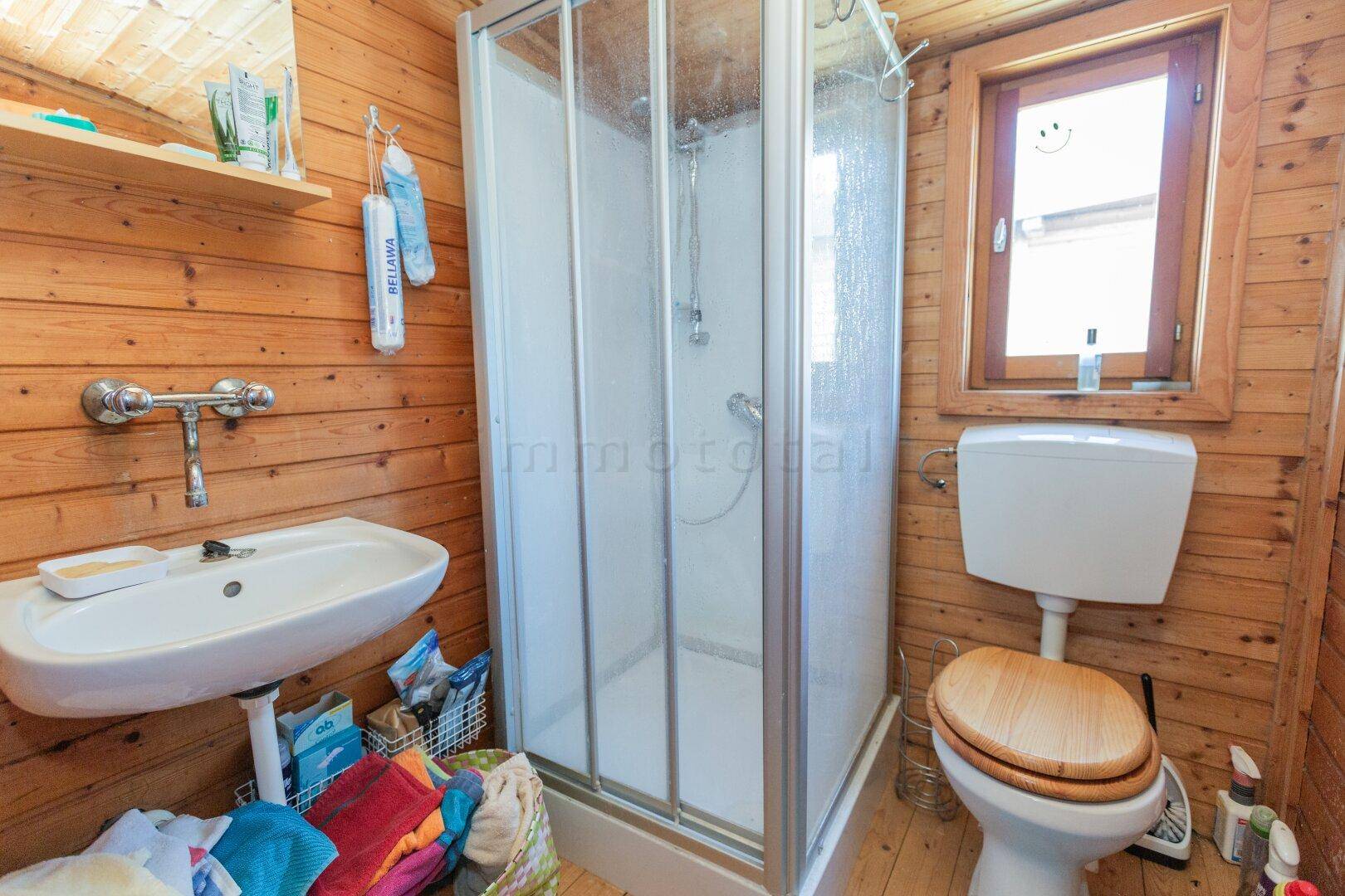 Kleines Badezimmer mit Dusche, WC, Waschbecken und Holztäfelung.