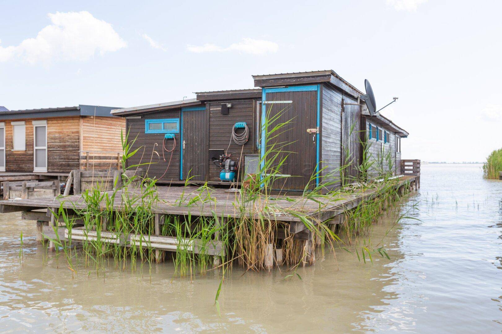 Seitenansicht eines Holzhauses auf Stelzen mit einem kleinen Anbau am See.