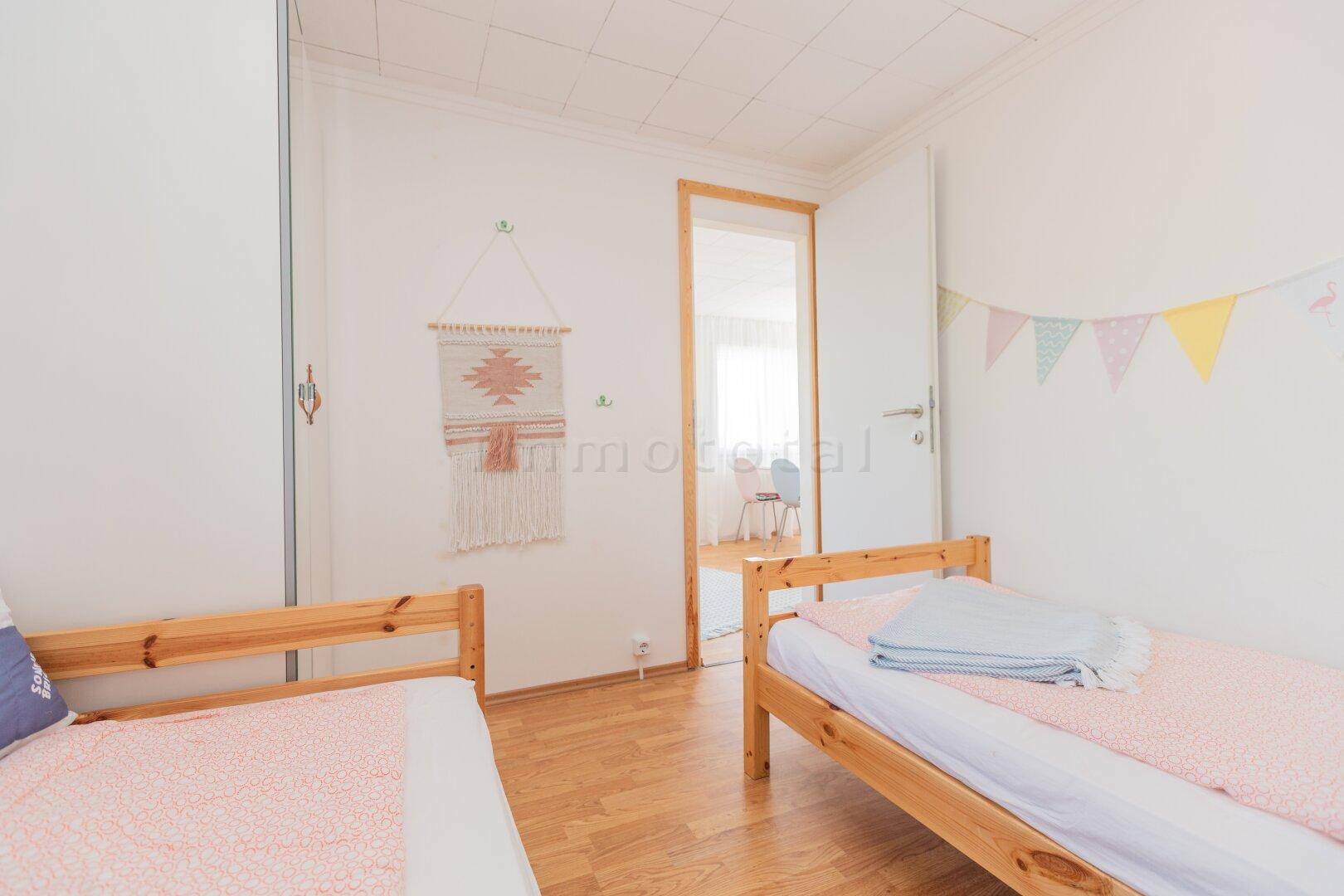 Helles Schlafzimmer mit zwei Einzelbetten und Zugang zu einem weiteren Raum.