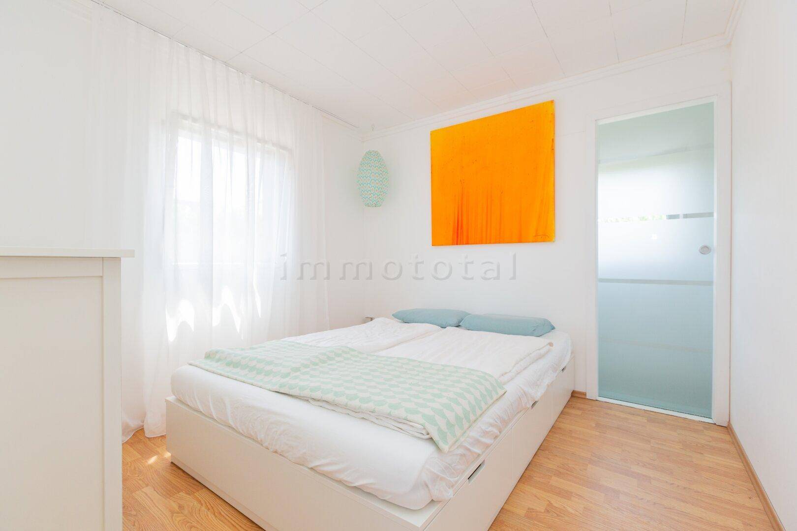 Schlafzimmer mit Doppelbett, farbenfrohem Kunstwerk und einer modernen Schiebetür aus Glas.