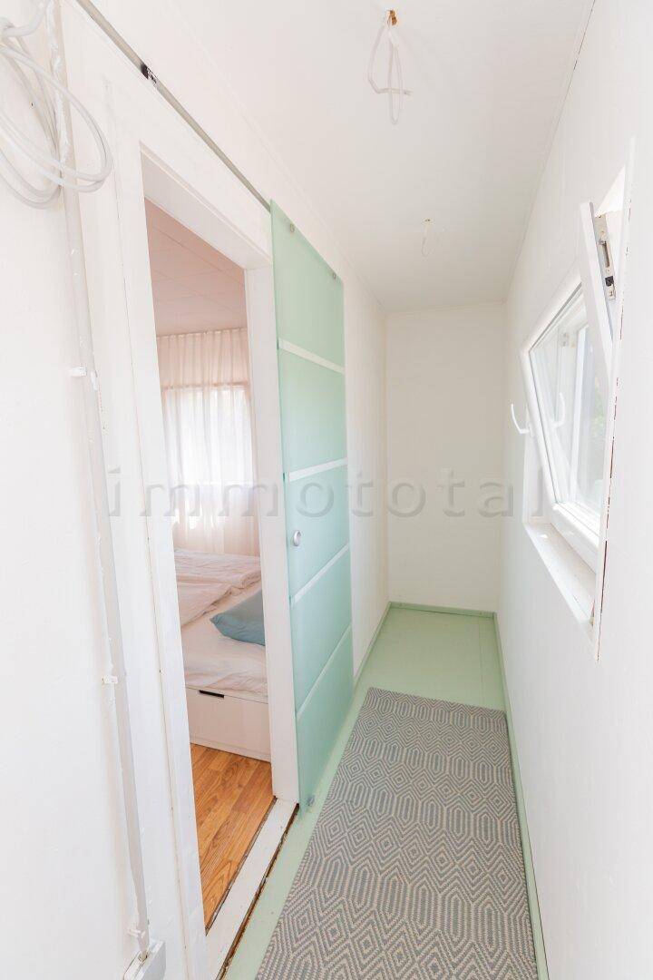 Schmaler Flur mit Fenster und einer modernen Schiebetür, die zum Schlafzimmer führt.