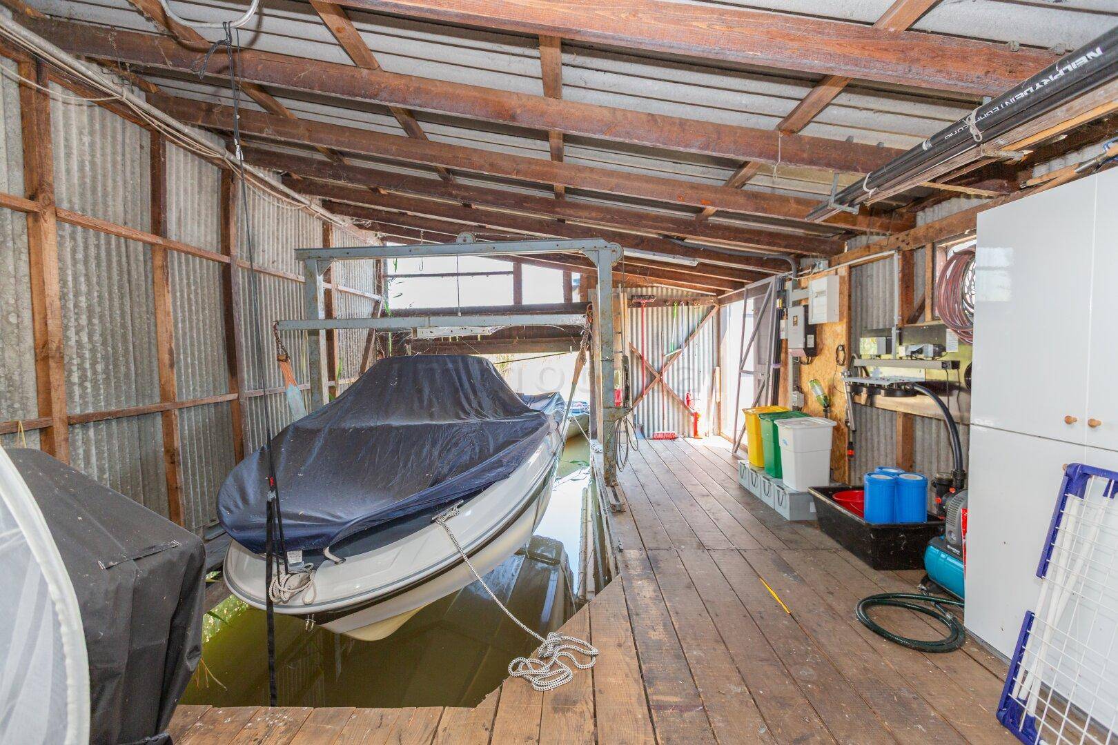Geräumiges Bootshaus mit einem Boot auf dem Lift, Holzboden und verschiedenen Geräten.