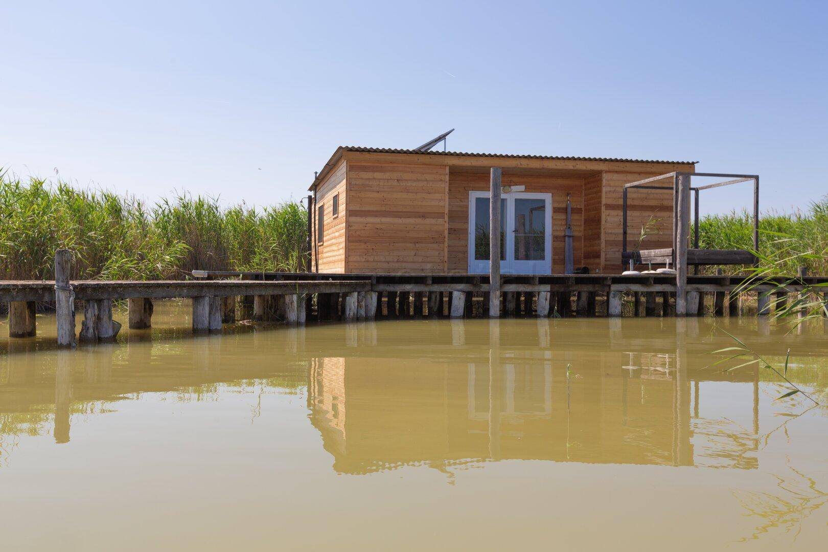 Charmantes Holzhaus auf Stelzen mit Wellblechdach und Solarpaneelen am Seeufer.