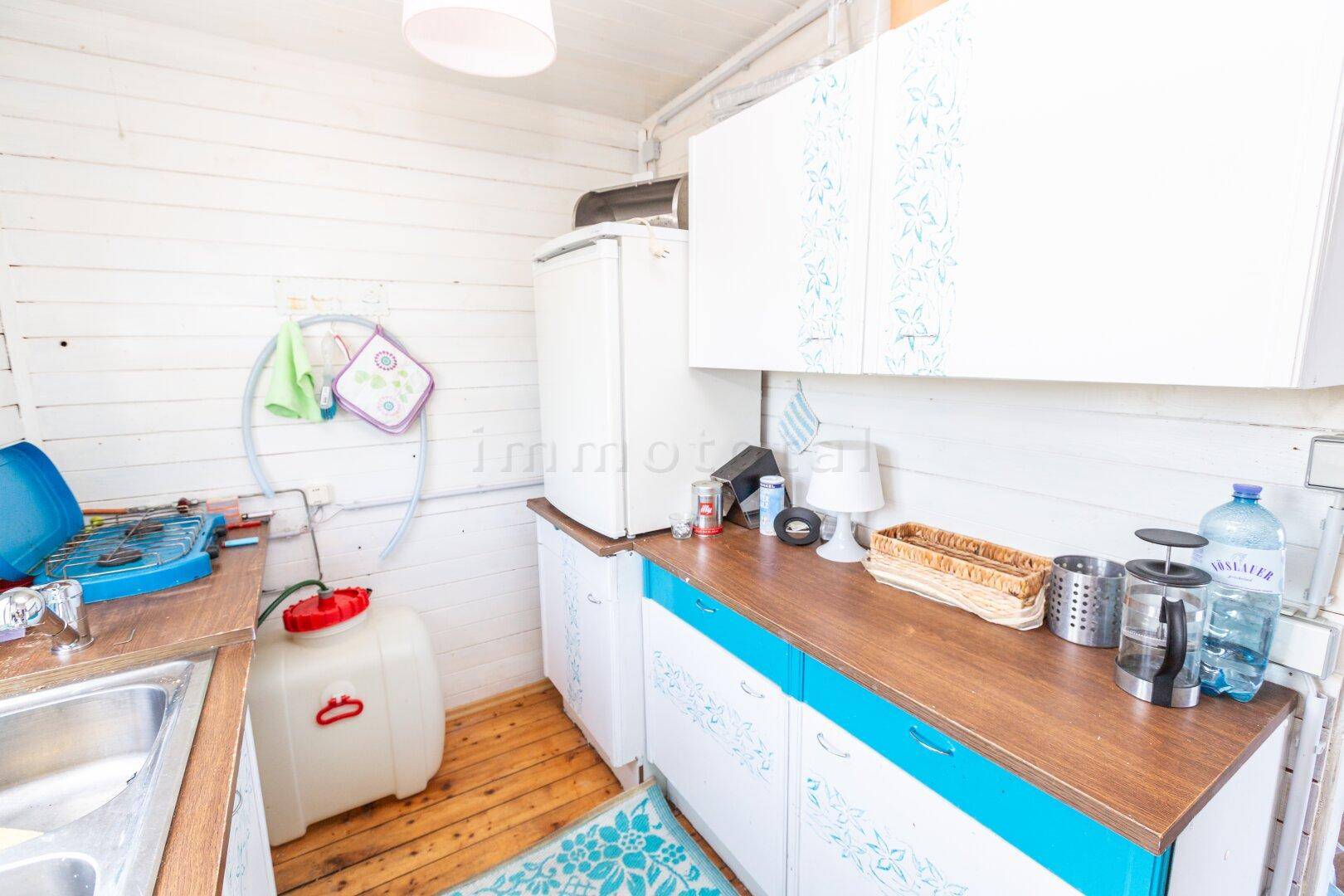 Einfache Küche mit Kühlschrank, Holztheke und weiß getäfelten Wänden in hellem Ambiente.