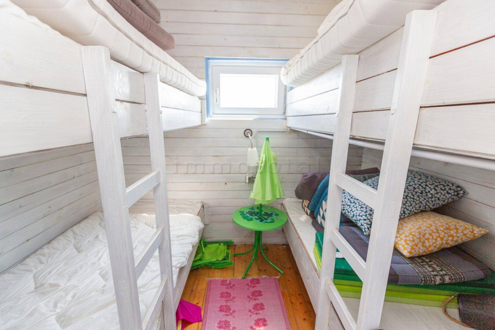 Kleines Schlafzimmer mit zwei Etagenbetten und einem Fenster, ideal für Kinder oder Gäste.