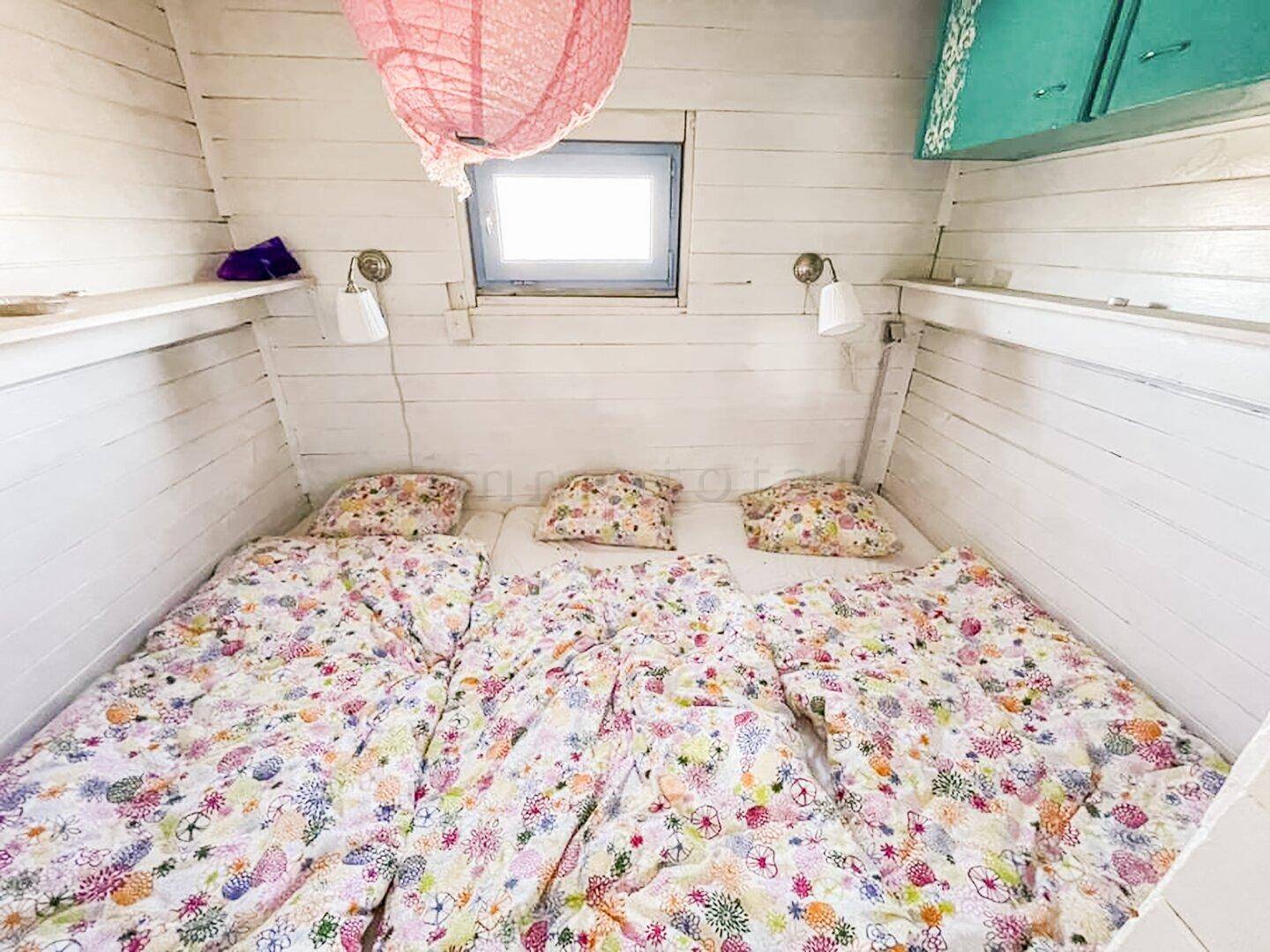 Gemütliches Schlafzimmer mit Doppelbett, floraler Bettwäsche und weiß getäfelten Wänden.