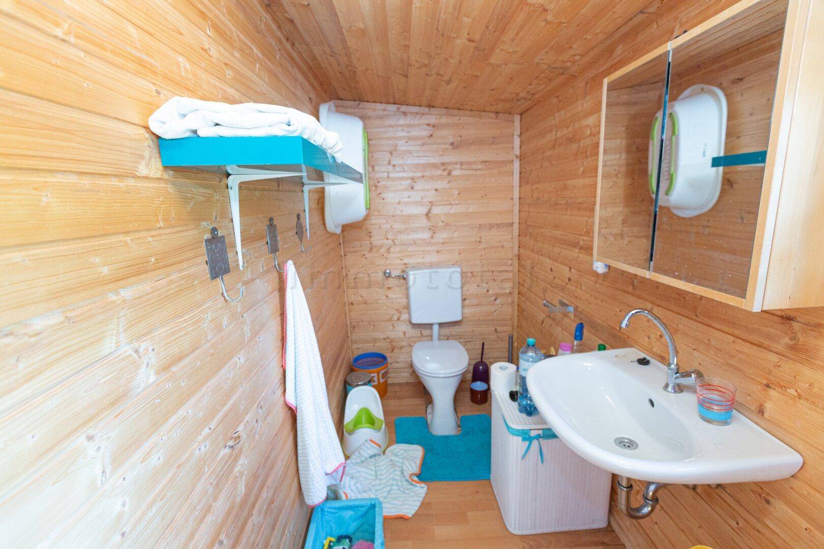 Einfaches Badezimmer mit Holzverkleidung, Toilette und Waschbecken, funktional eingerichtet.