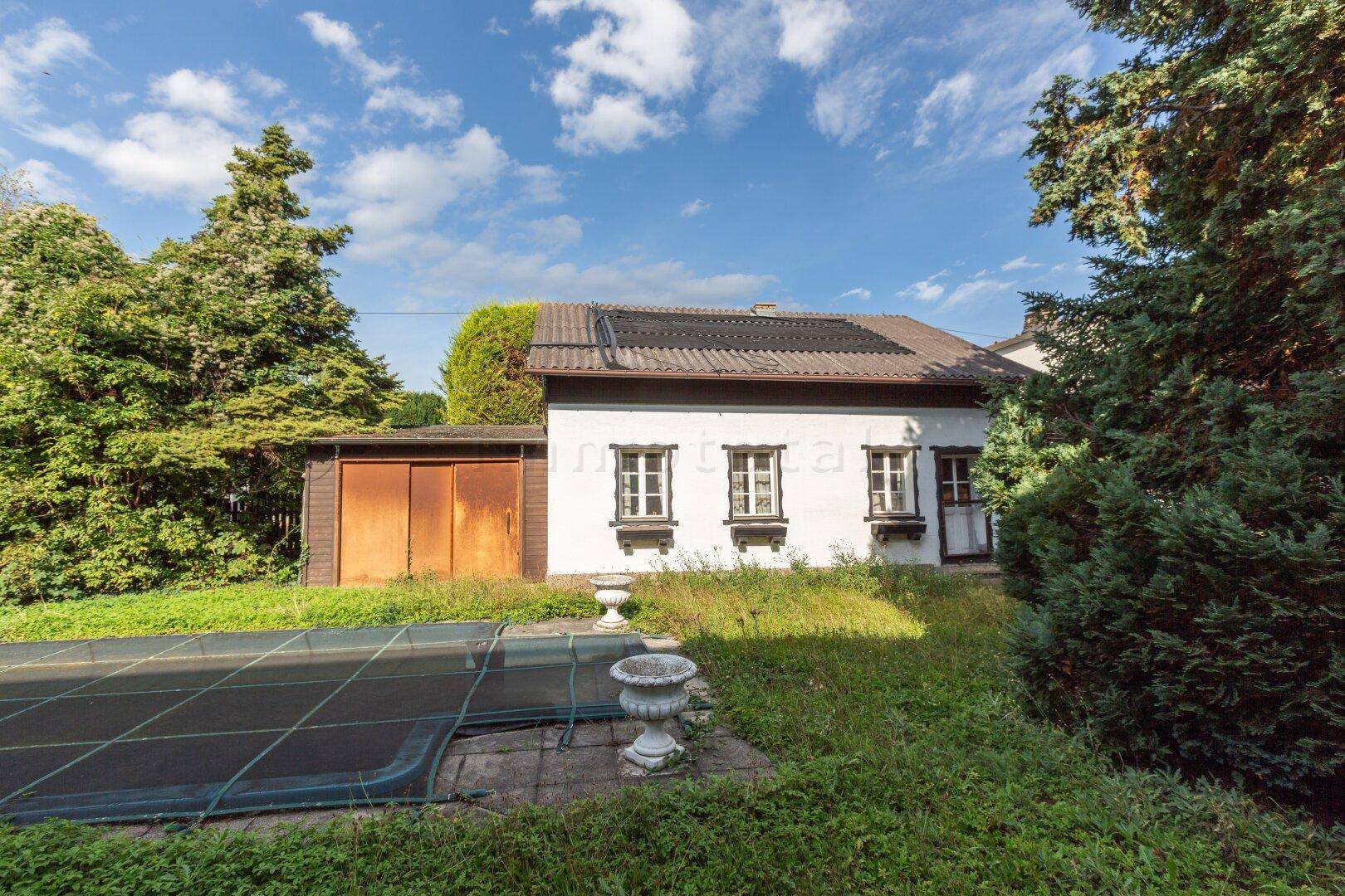 Hinteransicht des Hauses mit einem abgedeckten Pool und altem Baumbestand im Gartenbereich.
