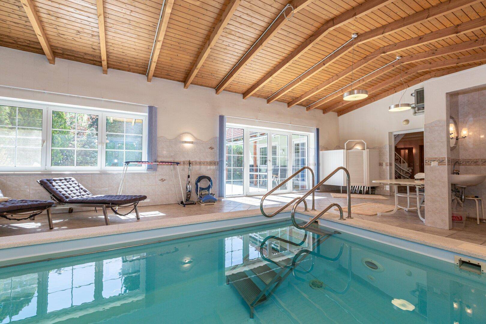 Geräumiger Innenpoolbereich mit Holzdecke, großen Fenstern und Liegestühlen zum Entspannen.
