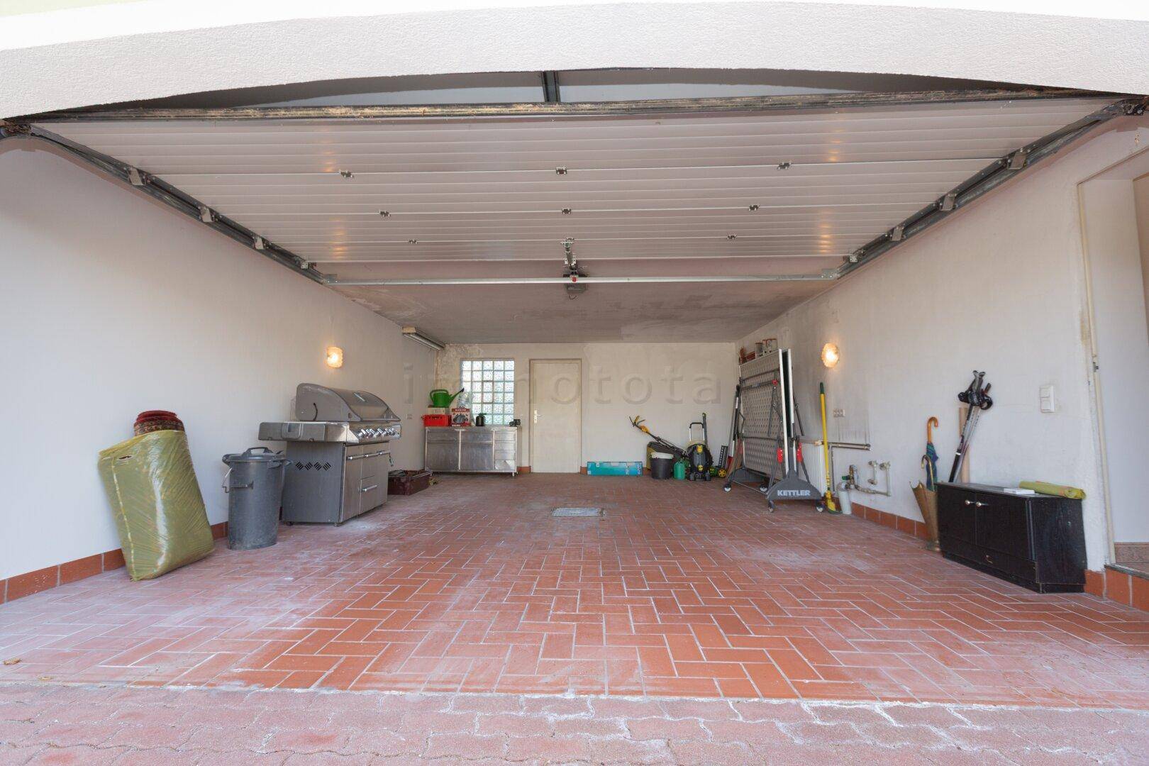 Geräumige Garage mit Ziegelboden und Platz für mehrere Fahrzeuge sowie Stauraum.