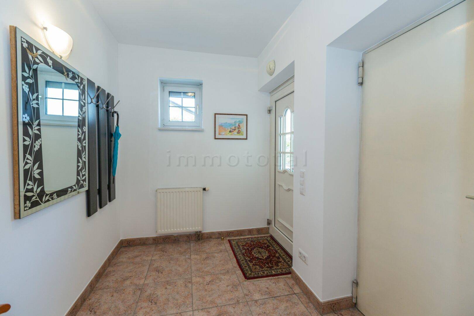 Heller Eingangsbereich mit Fliesenboden, kleinem Fenster und Garderobe.