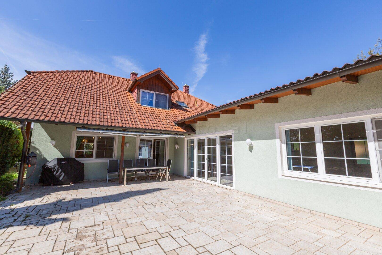 Rückansicht des Hauses mit großer Terrasse, Garten und Dachgauben.