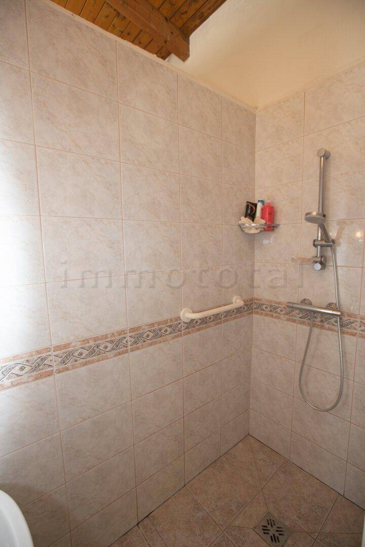 Geflieste Dusche mit Haltegriff und Duschkopf, ideal für Barrierefreiheit.