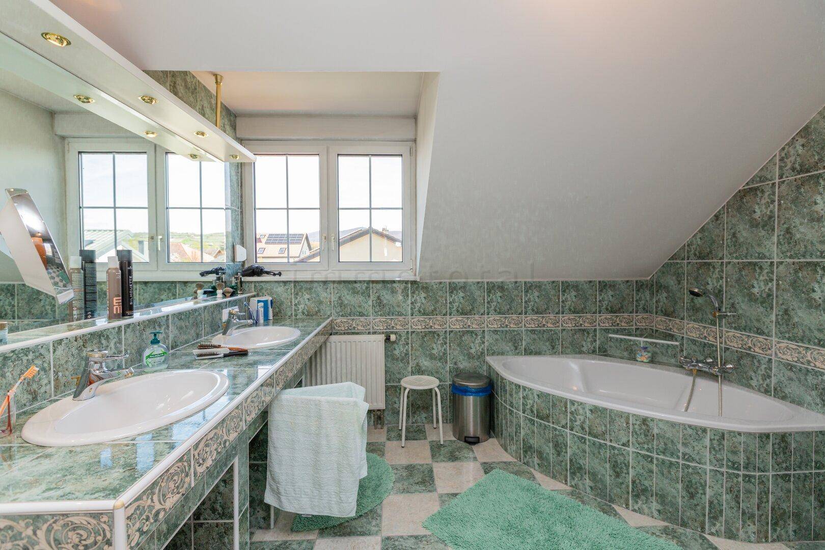 Geräumiges Badezimmer mit grünen Fliesen, Doppelwaschbecken und Eckbadewanne.