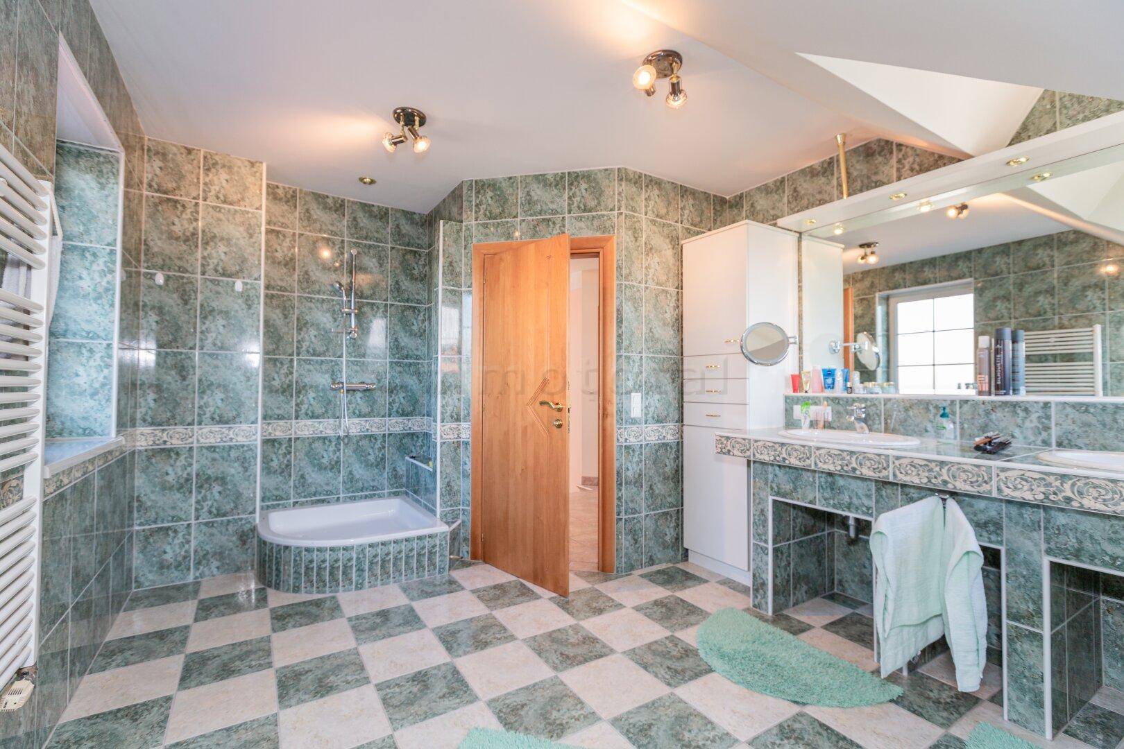 Großes Badezimmer mit grünen Fliesen, Dusche und Doppelwaschbecken.