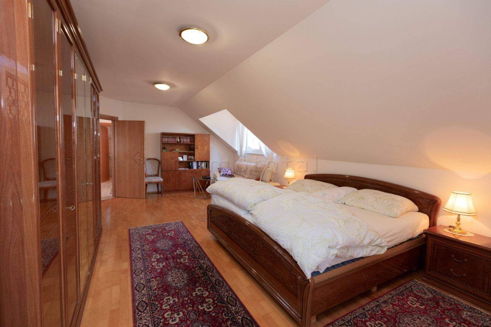 Schlafzimmer im Dachgeschoss mit Holzboden, großem Bett und Kleiderschrank.