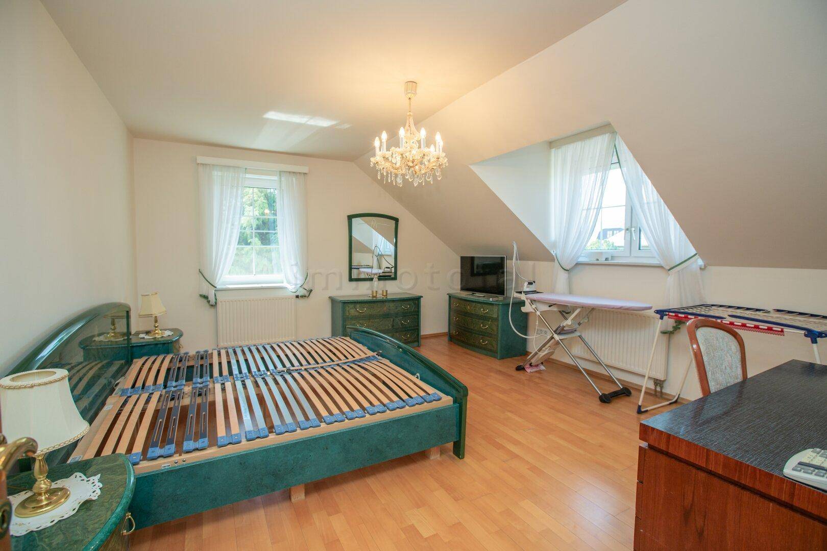 Helles Schlafzimmer im Dachgeschoss mit Holzboden und Kronleuchter.