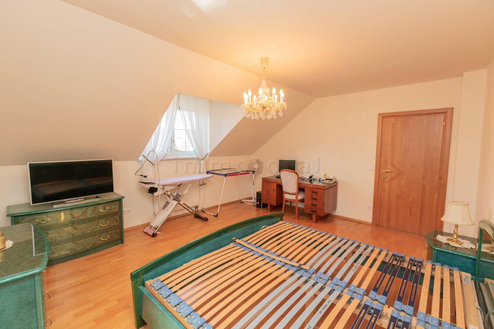 Schlafzimmer im Dachgeschoss mit Holzboden, Schreibtisch und Fernseher.